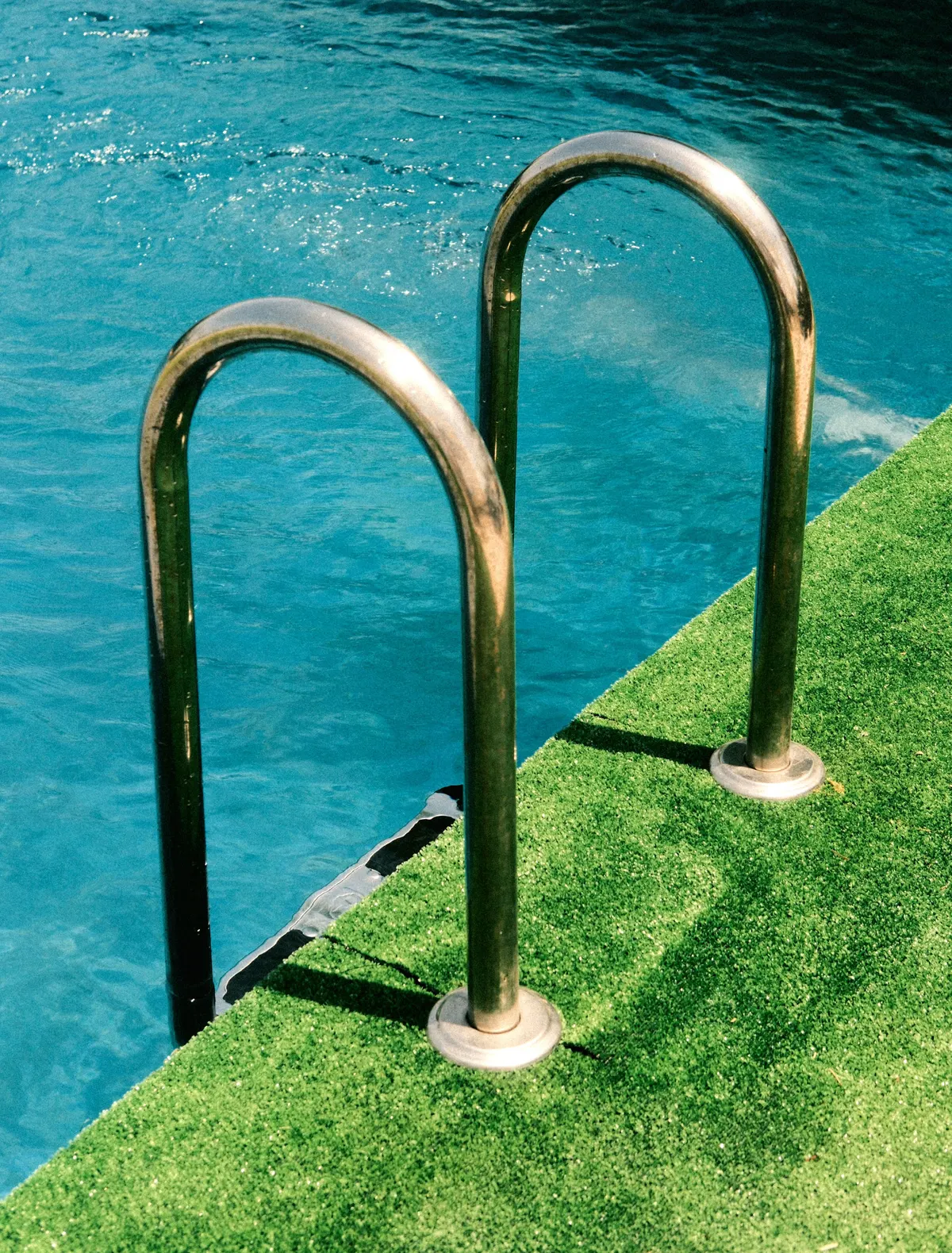 Artificial grass running up to the coping of a swimming pool with a steel ladder