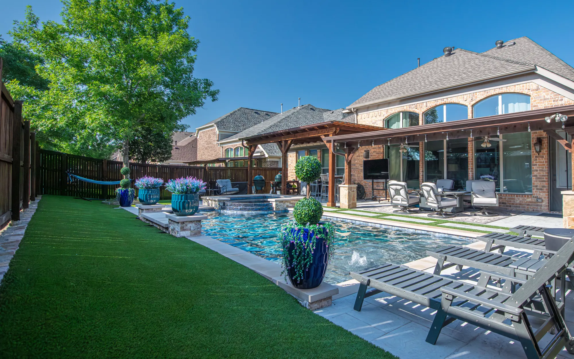 Backyard with an artificial turf lawn beside a swimming pool and a covered patio