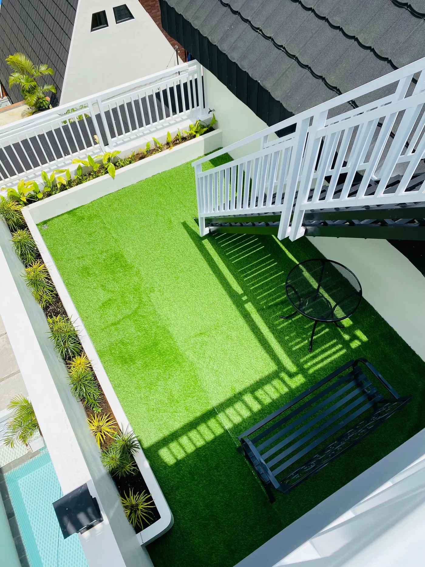 Overhead view of a rooftop terrace with artificial turf, planters, and a cafe table